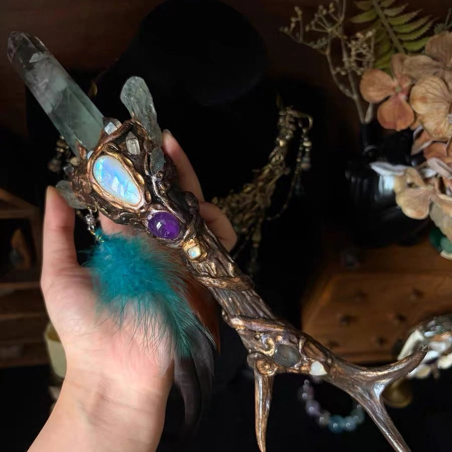 Side view of a natural antler crystal scepter with hand-painted details and a teal feather charm